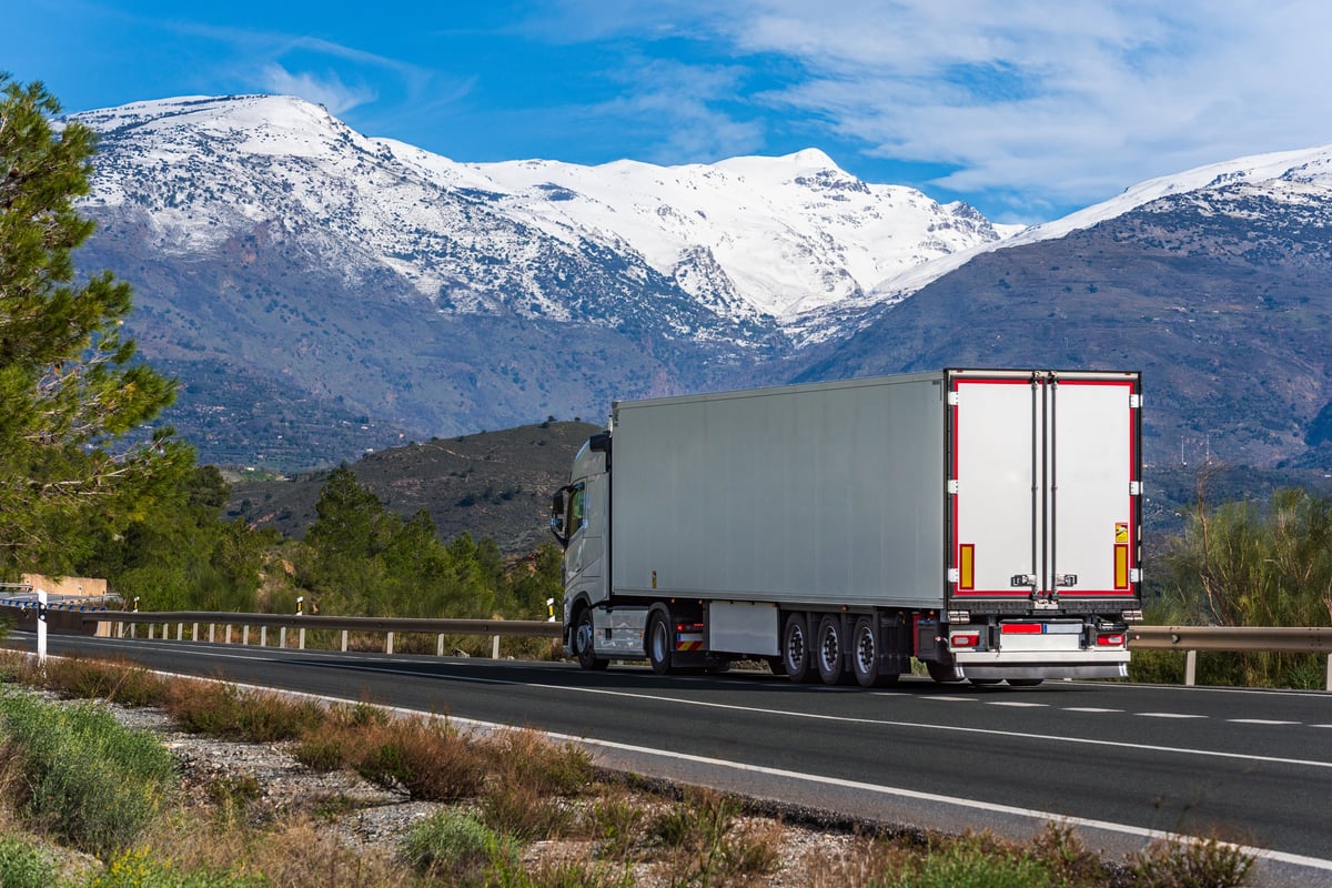 Refrigerated semi truck driving through a winter mountain landscape